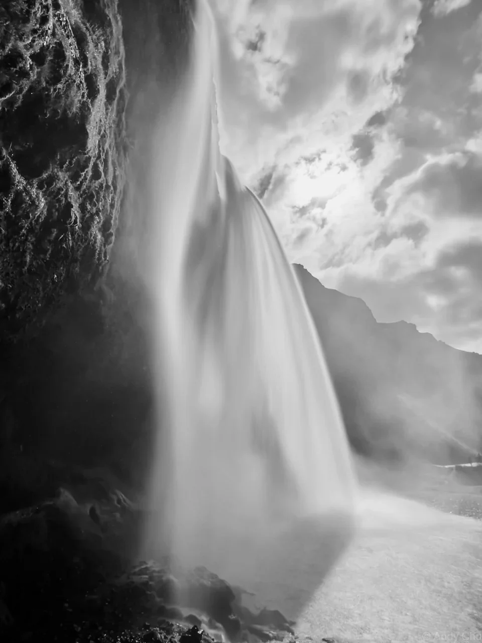 Black-and-white view looking up beside a tall waterfall