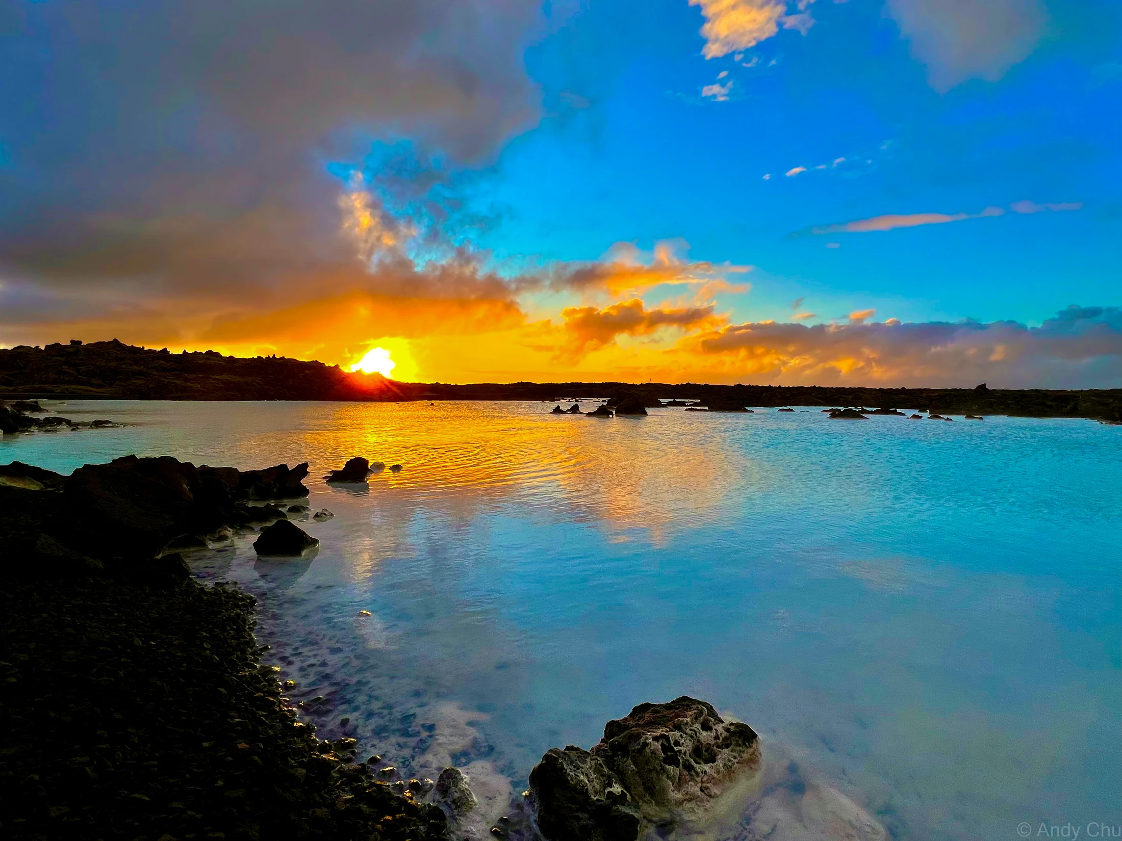 Sun setting over pale blue water and dark volcanic rocks