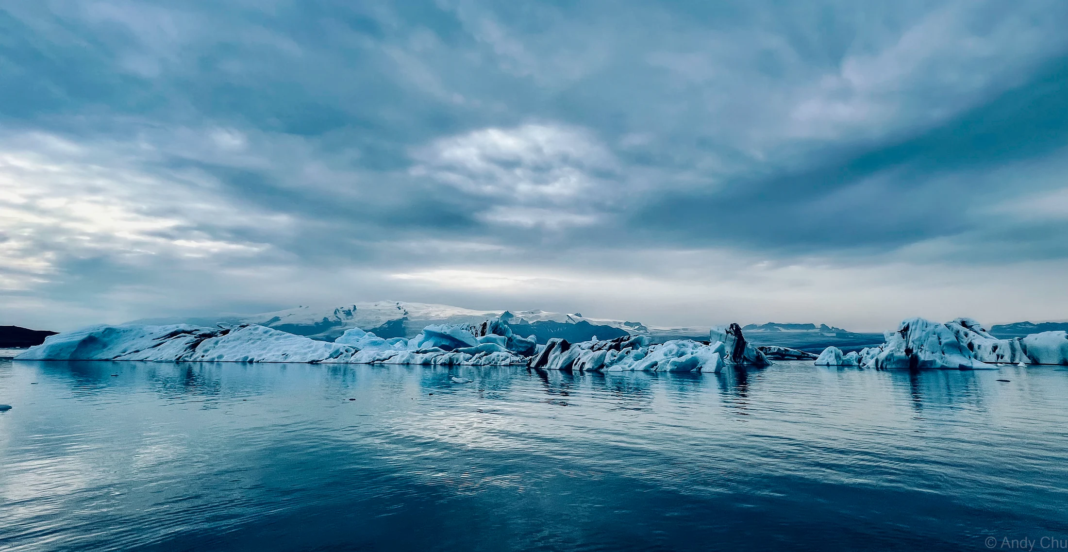 Blue glacial ice floating on calm water beneath a cloudy sky