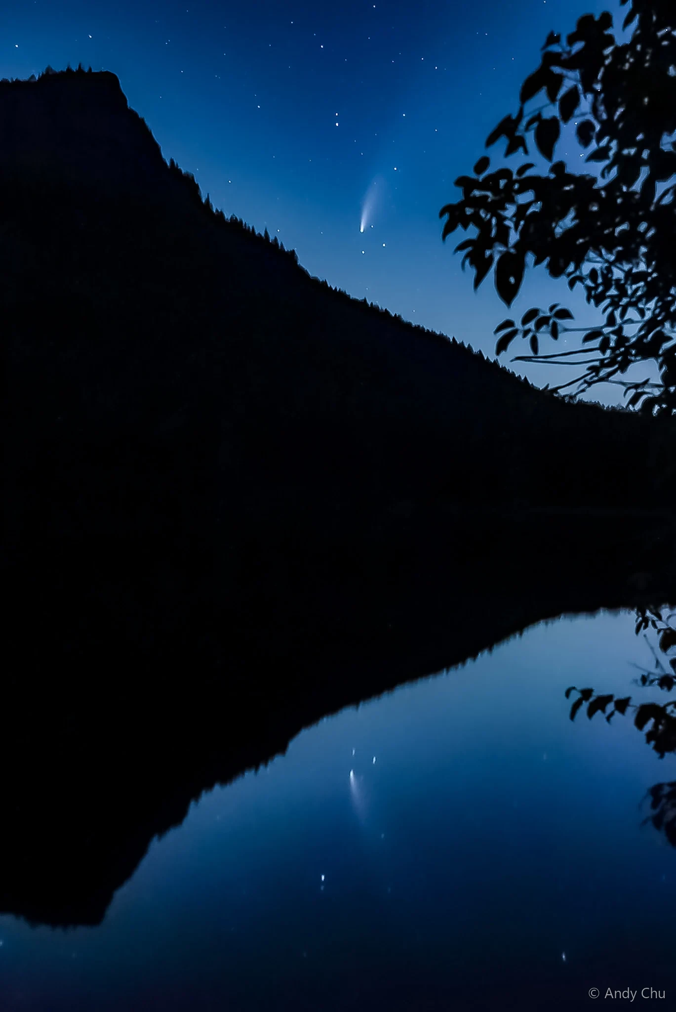 Comet above a dark mountain and its reflection in still water