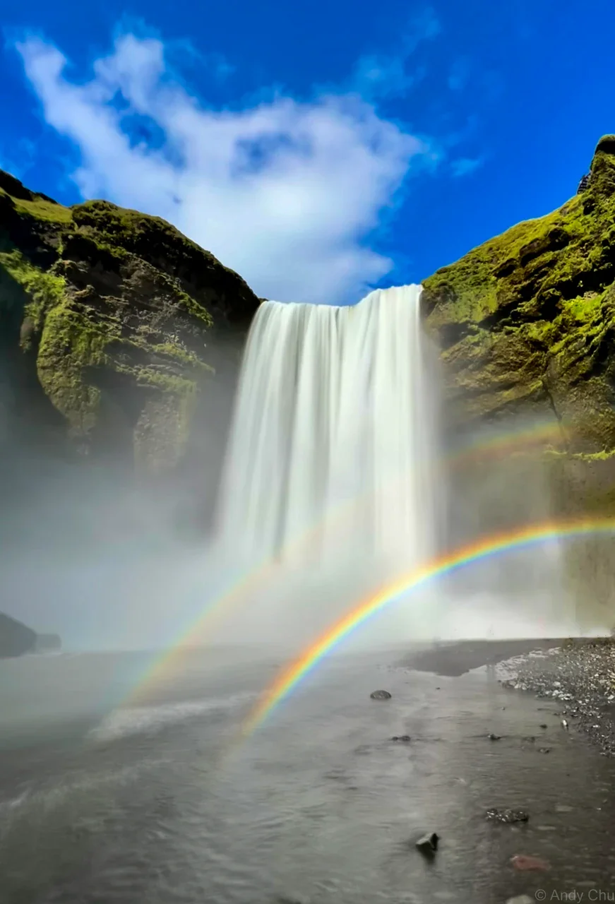 Tall waterfall beneath blue sky with a rainbow in the spray