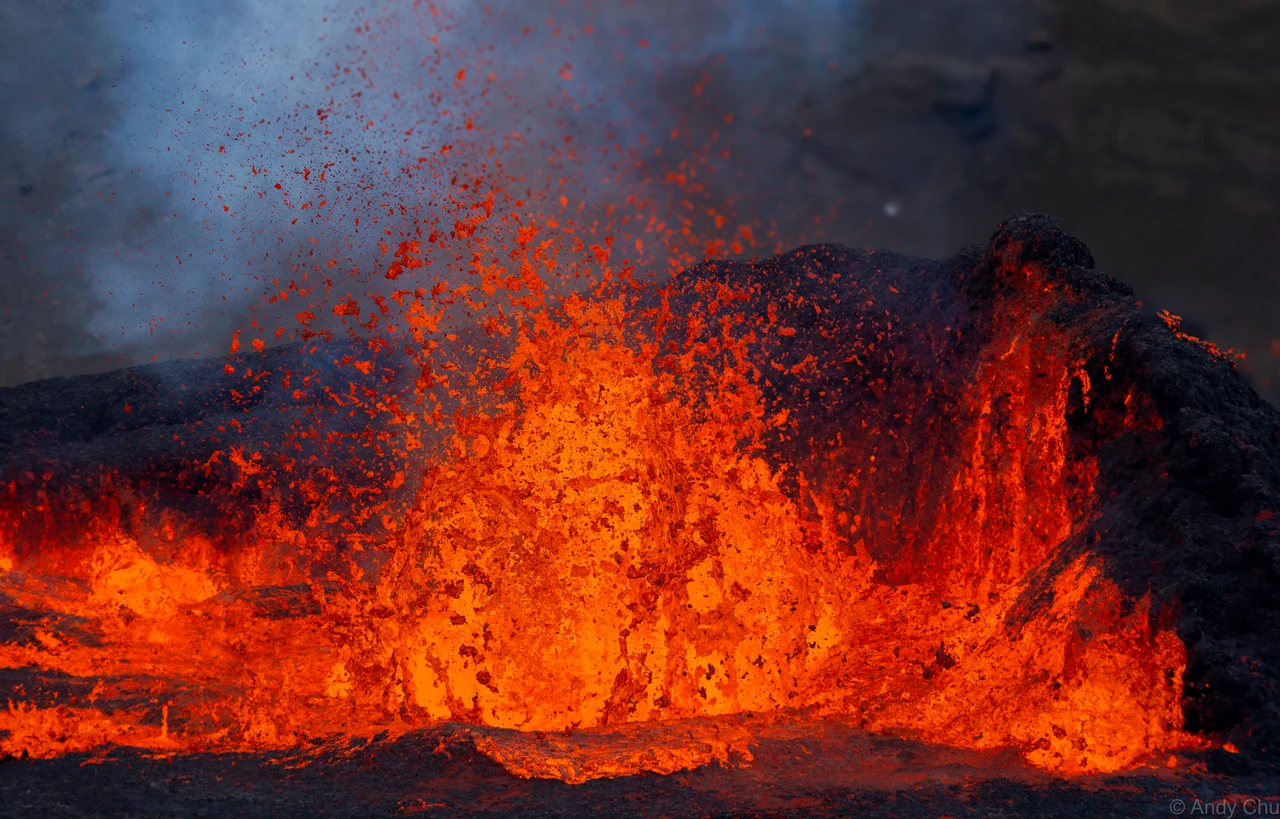 Orange lava erupting against dark rock and a grey sky