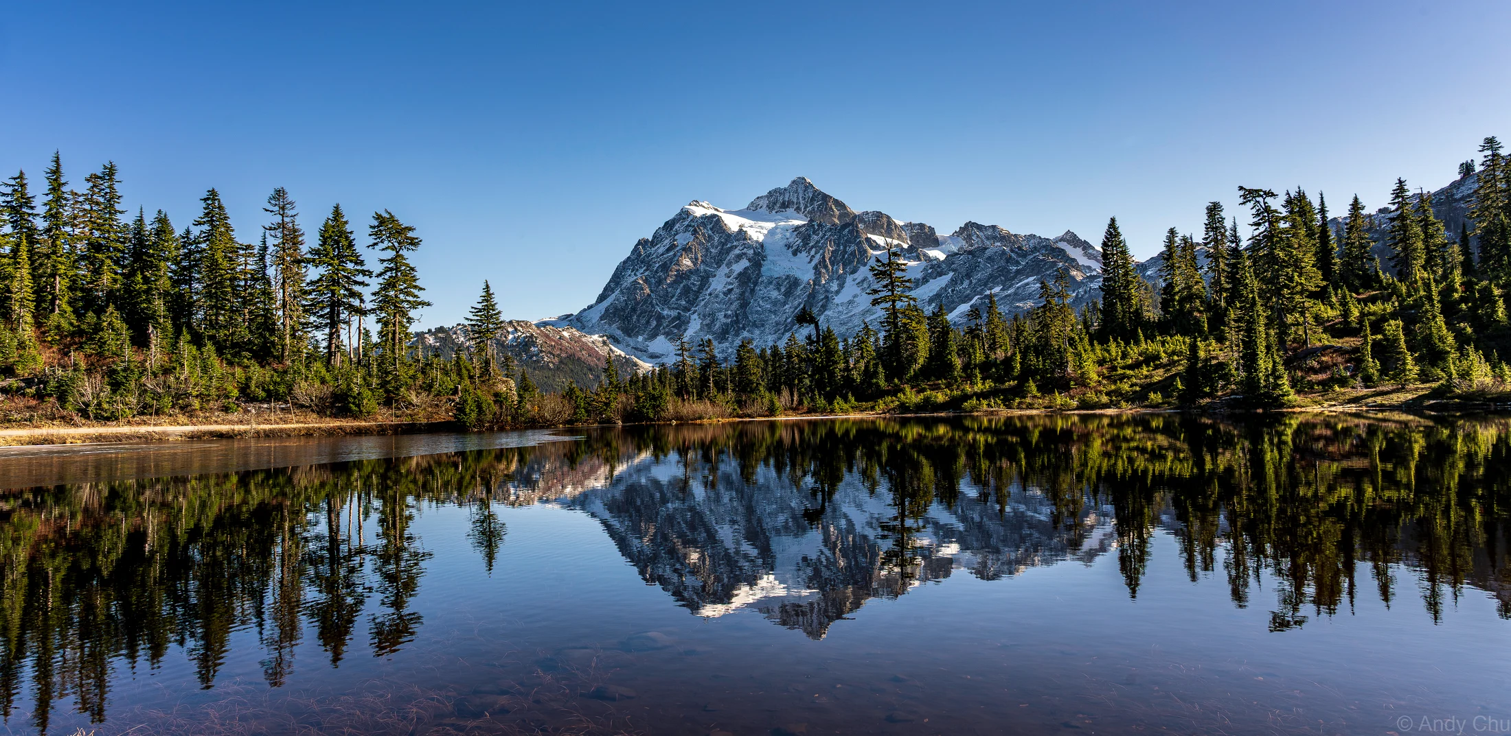 Mount Shuksan and evergreen trees reflected in still lake water